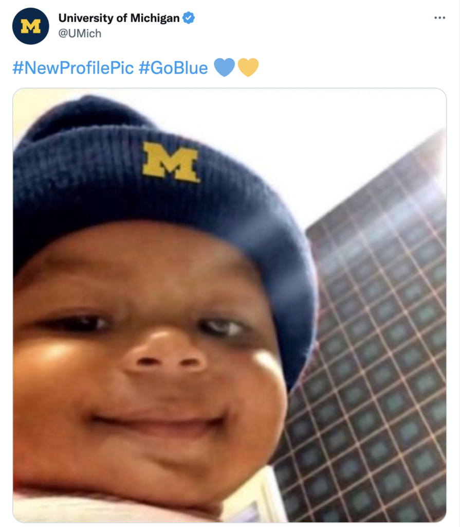 A baby wearing a Michigan hat smiling at the camera